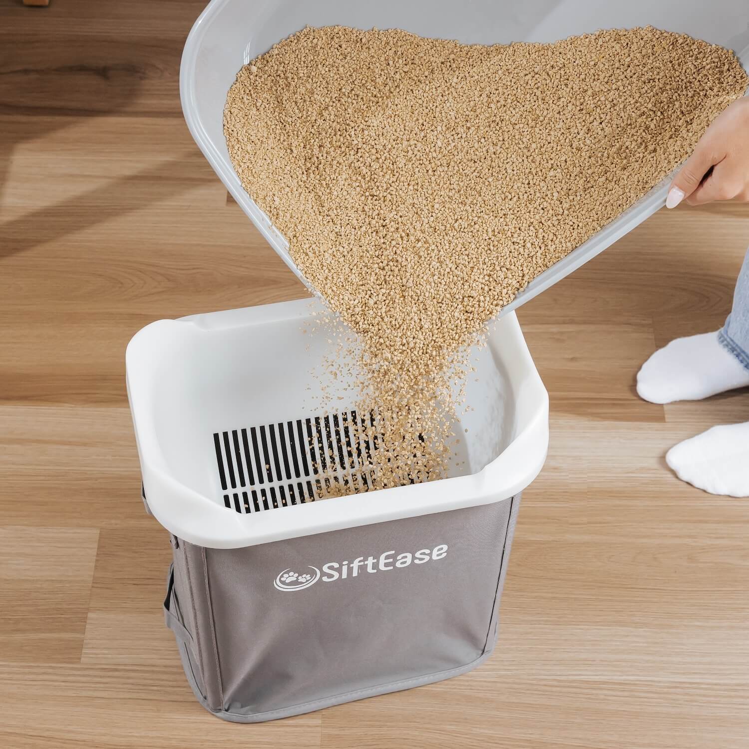 The SiftEase litter box sifter is compatible with any clumping litter, shown pouring and sifting corn litter.
